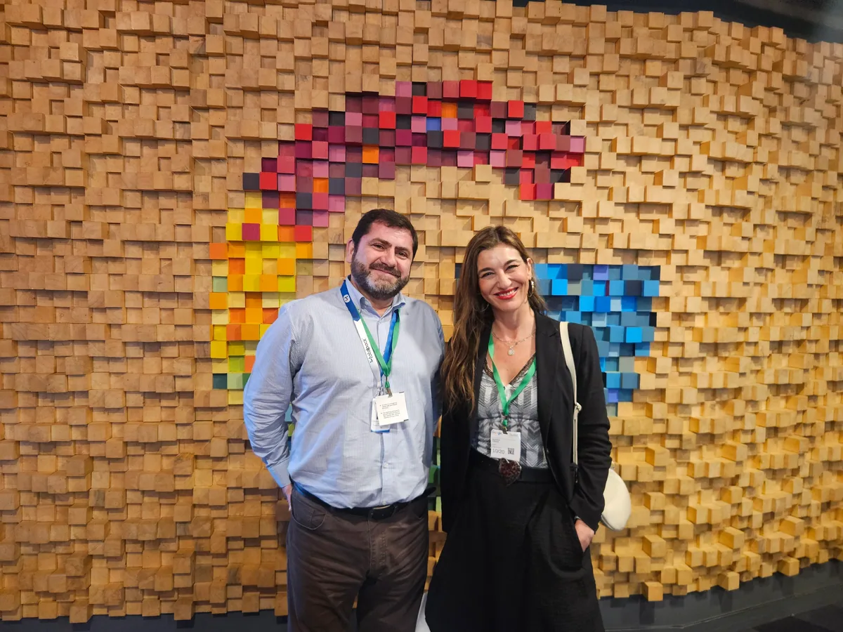 Un asistente y una asistente sonríen frente al muro de madera de colores de Google Santiago.