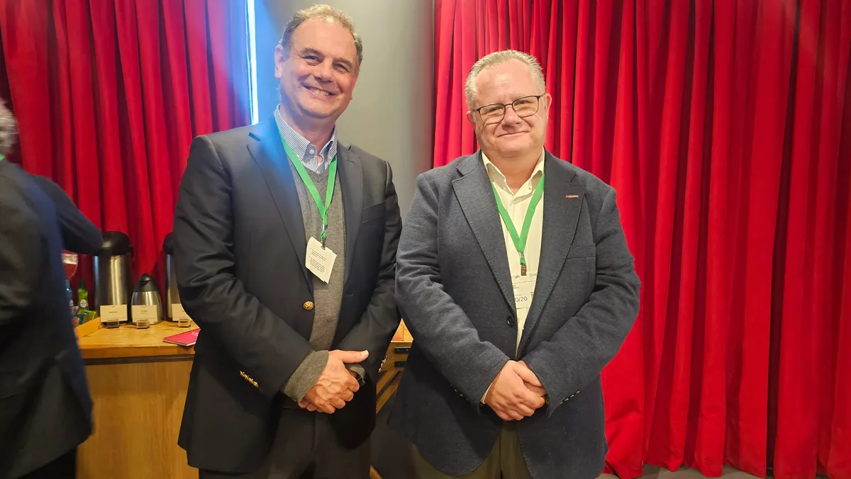 Dos asistentes sonríen y posan frente a la cortina roja durante el networking.