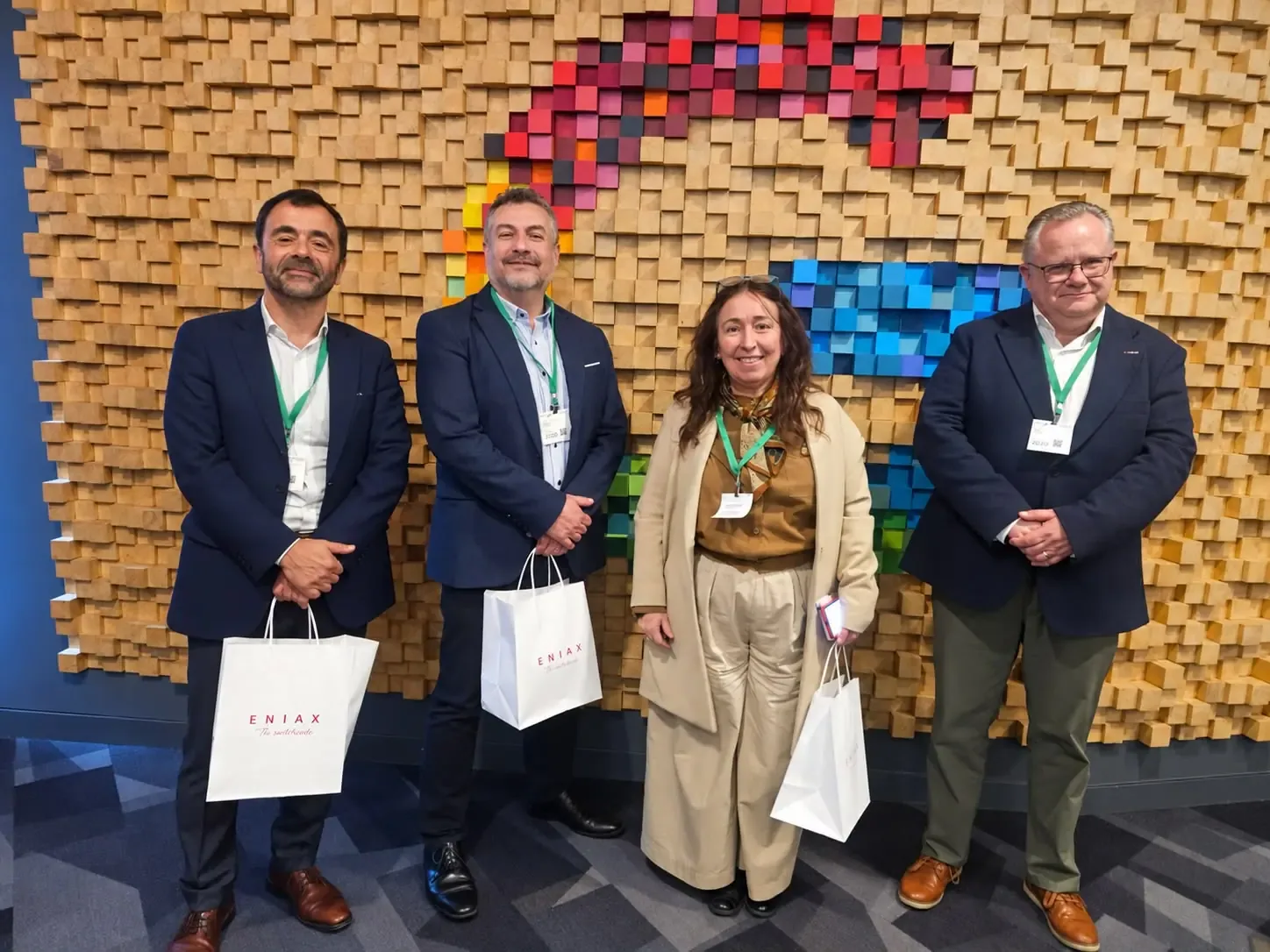 Cuatro participantes de la jornada frente al muro de madera de colores de Google Santiago, con bolsas de Eniax.